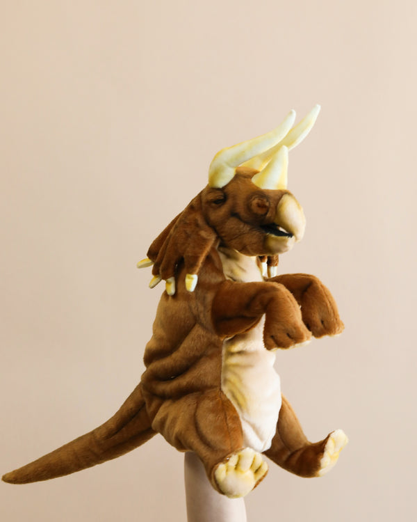 A Triceratops Puppet resembling a brown dinosaur with long arms and a yellow crest on its head, crafted from high-quality materials, standing against a plain, light-colored background.