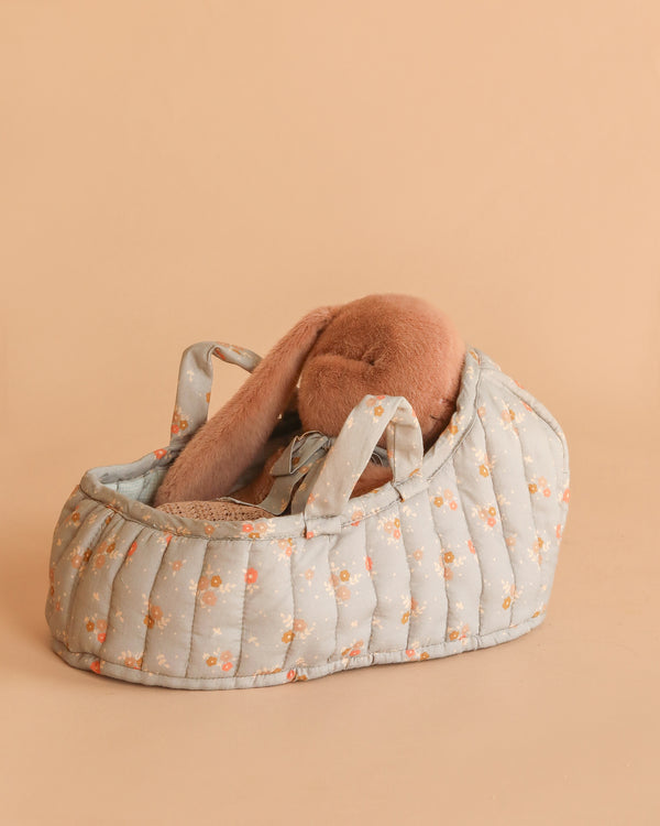 The Maileg Sleeping Bunny in Carry Cot features a soft brown plush bunny with long floppy ears, nestled in a small, padded carry cot decorated with a light blue floral pattern on a beige background.