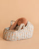 The Maileg Sleeping Bunny in Carry Cot features a soft brown plush bunny with long floppy ears, nestled in a small, padded carry cot decorated with a light blue floral pattern on a beige background.