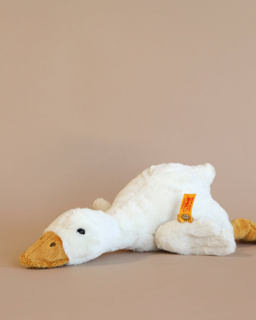 A Goose Stuffed Plush Animal lying on its side against a plain beige background, with a Steiff Button in Ear visible on its wing. The duck has a white body and an orange beak.