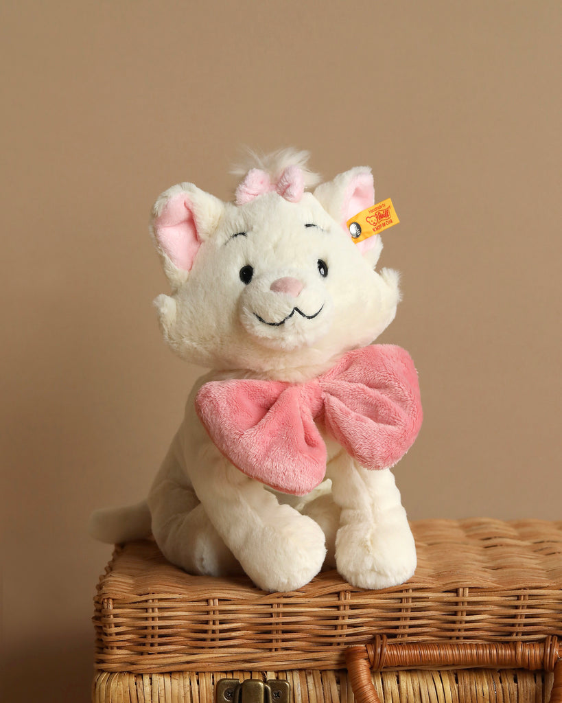 A young girl with light brown hair, wearing a long-sleeved pink shirt and beige pants, is sitting and hugging a Steiff, Disney's "Aristocats" Marie Cat Plush Stuffed Toy, 9 inches. She is looking down at the toy with a gentle and affectionate expression. The background is neutral and softly lit.