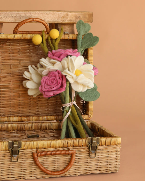 The Handcrafted Felt Flower Bouquet features white, pink, and yellow blooms with green leaves in an open wicker picnic basket, set against a beige background for a charming and sustainable touch.