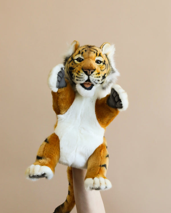 A hand-sewn Tiger Puppet being held up against a plain beige background, with its paws playfully raised.
