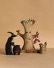 The Bumbu Handmade Witch with Cauldron and Haunted Tree Set features a wooden witch stirring her cauldron beside two tree figures, creating a charming Montessori Waldorf display against a simple beige background.