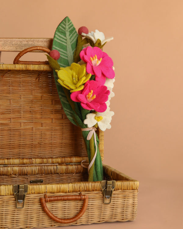 The Handcrafted Felt Flower Bouquet, featuring vibrant wool-felt blooms and green leaves, sits inside an open wicker picnic basket against a solid beige background.