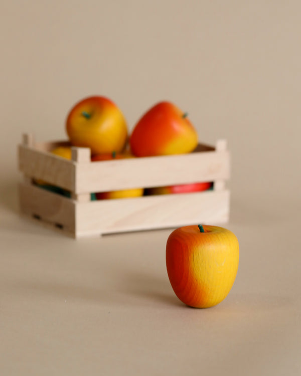 A small handcrafted wooden crate containing several Erzi Yellow-Red Apple Pretend Foods on a plain background, with one Erzi Yellow-Red Apple Pretend Food in front of the crate. All items are depicted in a simple, minimalistic style.