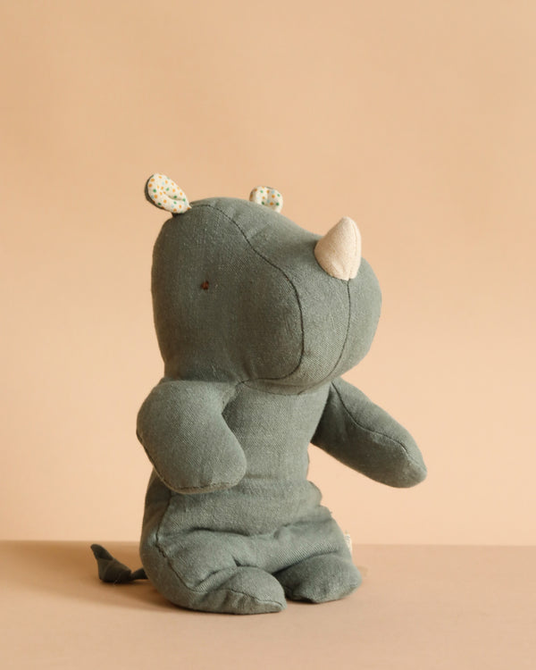 The Maileg Small Rhino - Pine is a soft, green stuffed toy made from recycled polyester, featuring a white horn and patterned inner ears, sitting upright against a beige background.