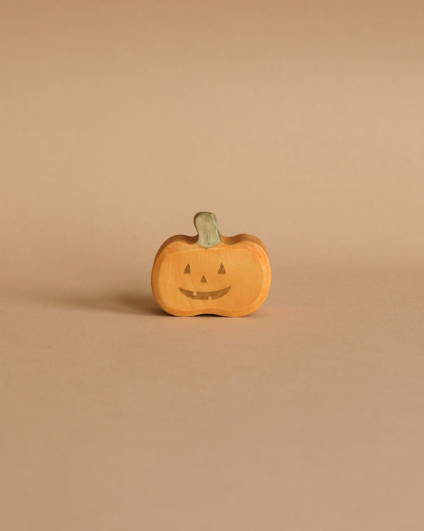 The Wooden Happy Jack-O-Lantern, a small, orange wooden pumpkin crafted from sustainable hardwood with a green stem and a carved smiling face, stands on a beige background. Its simple design gives it a cute and minimalist Halloween appearance, reminiscent of a classic Jack-O-Lantern.