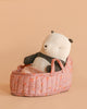The Maileg Panda Bear in Carry Cot rests comfortably in a pink, floral-patterned basket against a plain beige background, appearing cozy and ready for nap time.