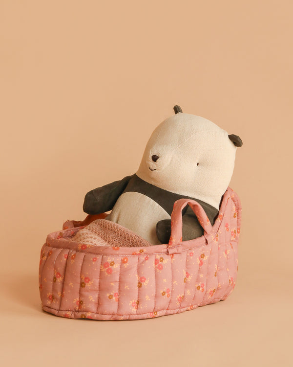 The Maileg Panda Bear in Carry Cot rests in a small, pink, floral-patterned cot against a plain beige background.