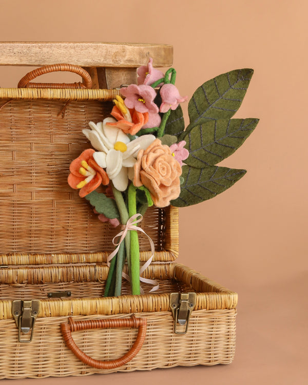 The Handcrafted Felt Flower Bouquet with green felt leaves sits in an open wicker basket and matching lid, displayed on a plain beige background.