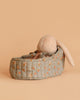 The Maileg Plush Bunny in Carry Cot features floppy ears and rests in a small, quilted floral bed against a warm dusty brown background.