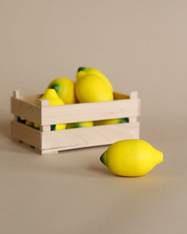 A small wooden crate containing several Erzi Lemon Pretend Foods, with one Erzi Lemon Pretend Food placed in front of the crate on a beige background, ideal for playtime stimulation.