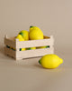 A small wooden crate containing several Erzi Lemon Pretend Foods, with one Erzi Lemon Pretend Food placed in front of the crate on a beige background, ideal for playtime stimulation.