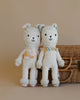 Two Cuddle + Kind Llama Stuffed Animals, one with a pink bow and the other with a green bow, made using hypoallergenic polyfill, standing arm in arm next to a wicker basket.
