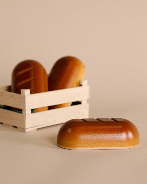 Three Erzi Bread Pretend Food soaps, one foregrounded and two in a small crate, handcrafted in Germany, set against a beige backdrop.