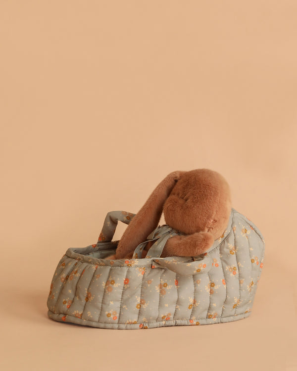 The Maileg Sleeping Bunny in Carry Cot features a cozy plush bunny tucked inside a floral-patterned carry cot, all set against a plain beige background.