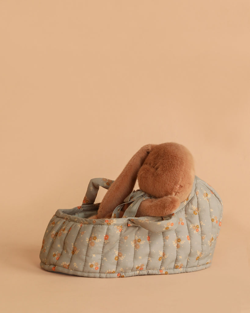 The Maileg Sleeping Bunny in Carry Cot features a cozy plush bunny tucked inside a floral-patterned carry cot, all set against a plain beige background.