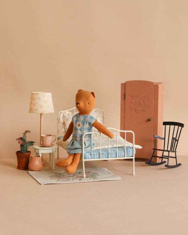 The Maileg Teddy Bedroom Set (ships in one week) features a Teddy Mum in a blue dress on a vintage bed, with a pink wardrobe, rocking chair, lamp, potted plants, cup, and teapot arranged on a rug.