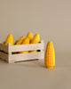 A wooden crate filled with several Erzi Corn on the Cob Pretend Foods with a prominent yellow and white patterned cob standing upright in front of it on a plain background.