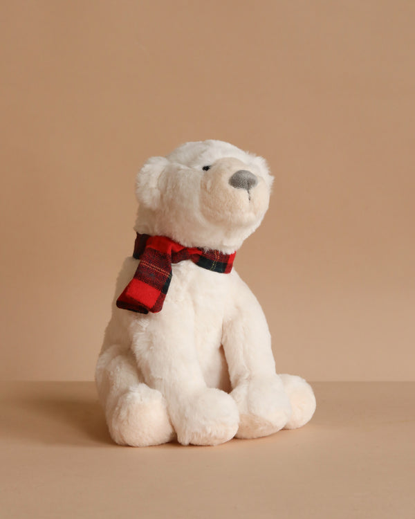 The Mon Ami - North Polar Bear Plush Toy, wearing a red and black plaid scarf, sits on a beige surface against a plain beige background.