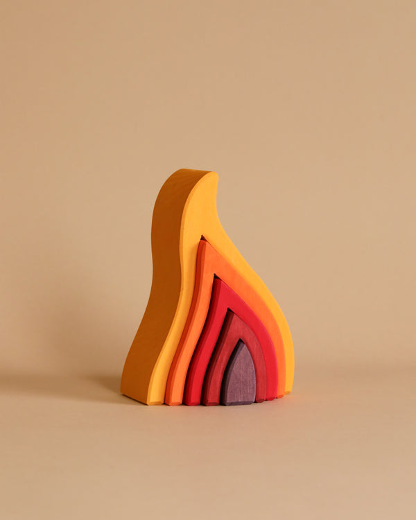 Introducing Grimm's Fire Stacker: a set of versatile, non-toxic wooden stacking blocks with flame-like shapes arranged together. Each piece is colorfully shaded in a gradient from yellow on the outside to a deep reddish-purple at the center, creating the illusion of a stylized fire. Perfect for children, this captivating set stands out against a neutral beige background.