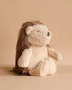The Mon Ami - Harlow Hedgehog Plush Toy, featuring soft, light brown fur and long, dark brown hair, sits upright against a beige background and faces slightly to the right.