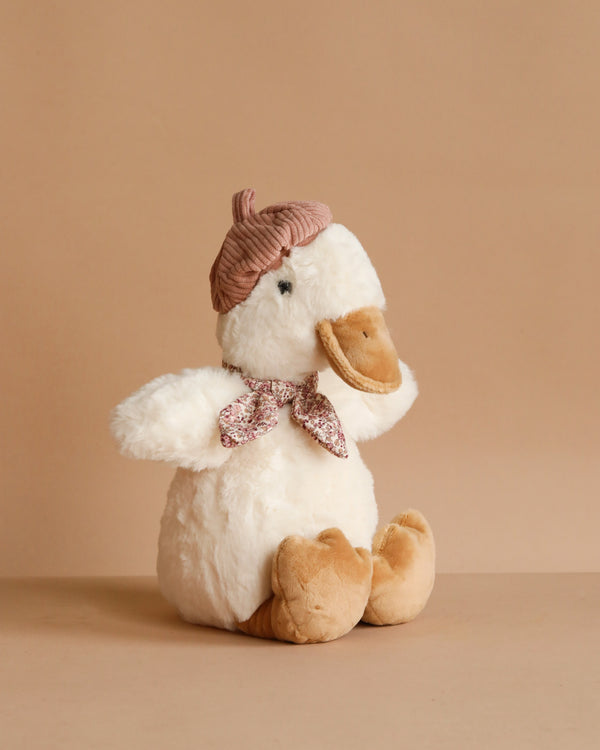 Mon Ami - Colette the Duck Plush Toy is a snuggly white duck with beige feet and beak, dressed in a pink knit hat and floral scarf, sitting against a plain beige background.