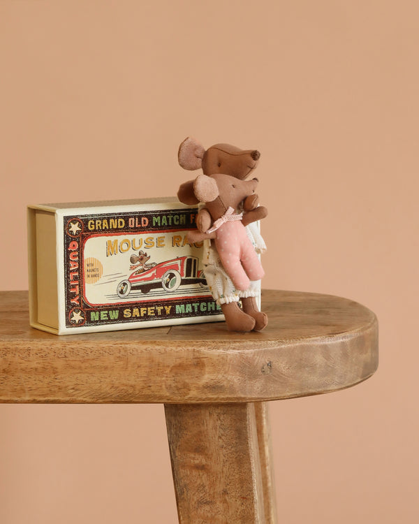 The Maileg Big Sister and Me Set features a mouse in a pink dress standing on a wooden stool beside a vintage-style "Mouse Race" matchbox, all set against a plain beige background.