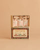 Three baby mice snuggle in patterned blankets inside the Maileg Triplets, Baby Mice in Matchbox - Checker set, featuring a soft beige background and a matchbox decorated with three cartoon mice in colorful pajamas.