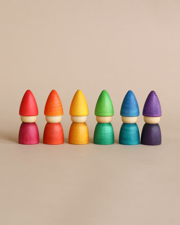 Six colorful, sustainable Grapat Rainbow Tomten figures lined up in a row, each consisting of a cone-shaped top and a rounded base, displayed against a plain, light beige background.