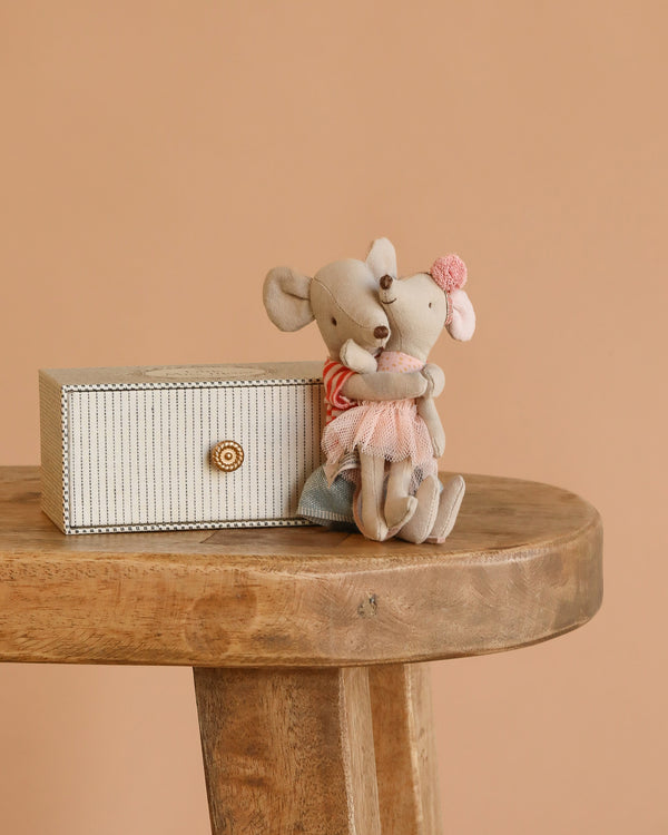 The Maileg Big Sister and Me Set features two charmingly dressed mice hugging on a wooden stool beside a small decorative box, all against a plain beige background.