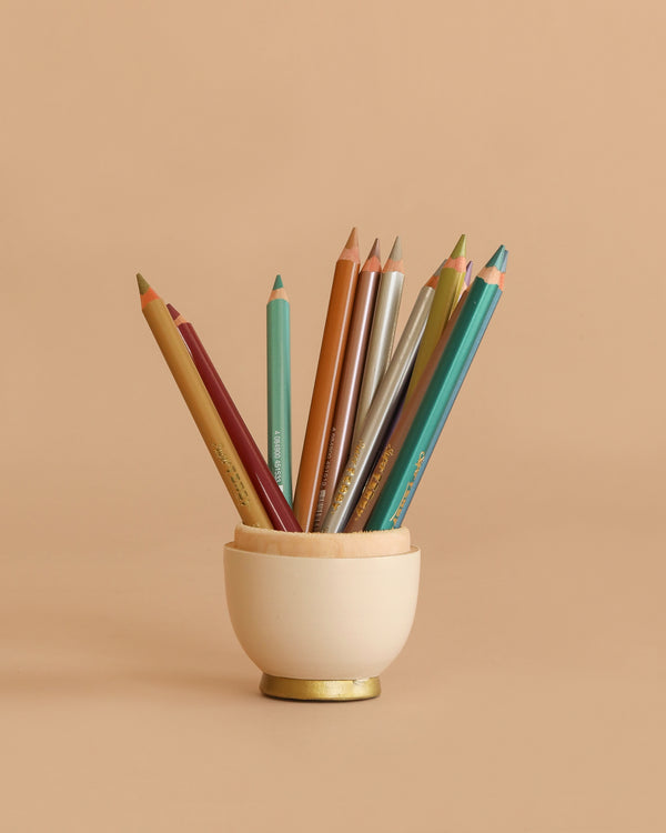 A small cream cup holds Lyra Pencils Super Ferby Lacquered Triangular—12 assorted metallic colors, including green, blue, gold, red, and brown—adding break-resistant shine to your creative space against a beige background.