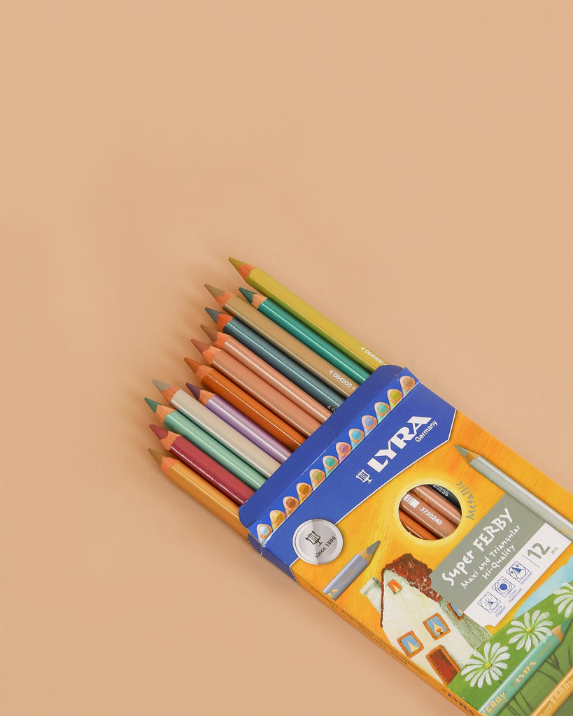 A partially open box of Lyra Pencils Super Ferby Lacquered Triangular - 12 Assorted Metallic Colors sits on a beige surface, showing break-resistant pencil tips through orange and blue illustrated packaging.
