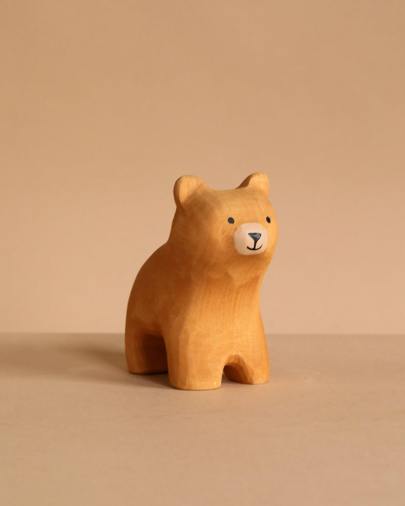 The Bumbu Handmade Wooden Bear and Forest Trees Set features a small, light brown bear figurine crafted from sustainably sourced wood, with simple painted details that invite sensory exploration against a neutral beige background.
