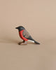 A Handmade Wooden Bullfinch Bird figurine painted with non-toxic water-based paint, featuring black, red, and white coloring on a light brown background. The bird is positioned sideways with its