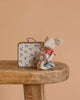 The Maileg Big Sister On the Go Suitcase Set features a small mouse in a red striped shirt and blue shorts holding a heart pillow, sitting beside a floral metal suitcase on a wooden table with a light brown background.