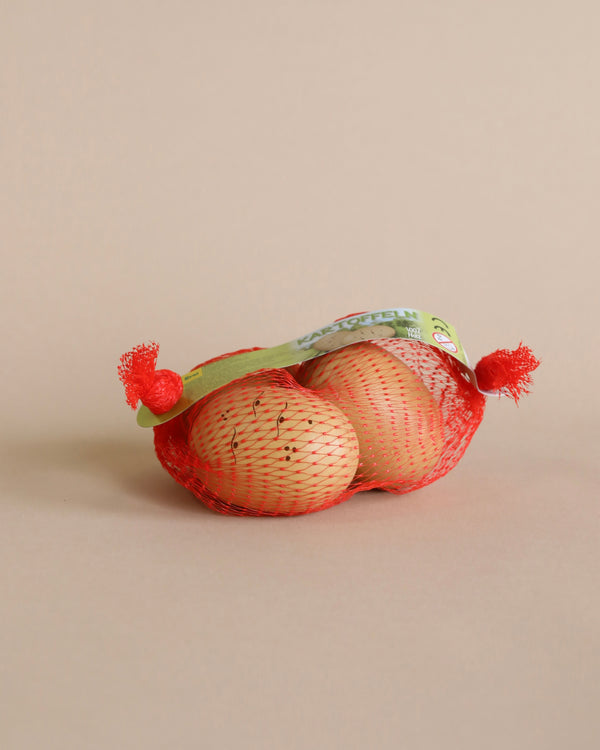 A pack of Potatoes in a Net Pretend Food with a green label, placed against a light peach background, labeled as "handcrafted in Germany.