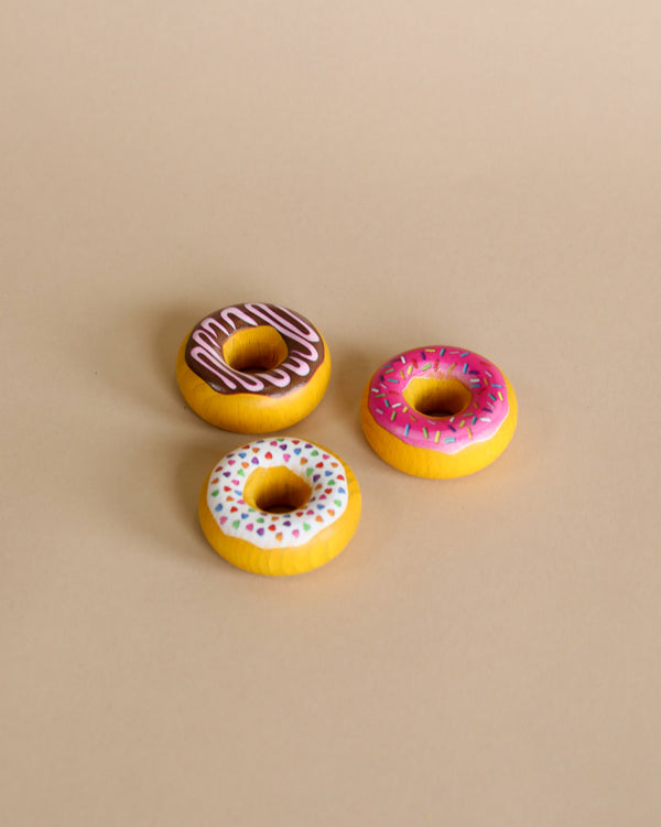 Three Erzi Doughnuts Pretend Food with various frostings and sprinkles, handcrafted in Germany, arranged on a plain beige background.