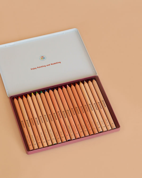 An open Stockmar Hexagonal Colored Pencil Set (18 Colors + Graphite Pencil) is arranged on a peach surface. The inside lid says, "Enjoy Painting and Modelling." Made in Germany with FSC certified wood.