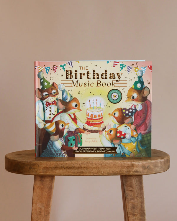 The Birthday Music Book is an interactive children’s storybook featuring illustrated mice in party hats around a birthday cake, shown upright on a wooden stool against a plain background.