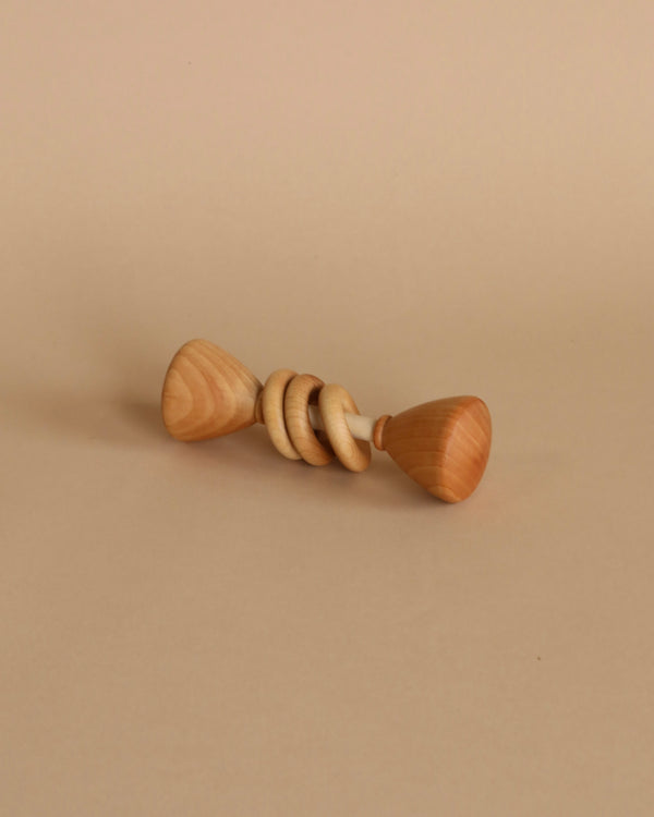 A wooden baby rattle, also suitable as a teething toy, with a twirled stick and spherical handle, lying horizontally on a plain beige background.