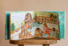 The Birthday Music Book is open on a wooden stool, displaying illustrated animals celebrating in a colorful, festive home. Both pages feature party scenes and sheet music inspired by classical masterpieces.
