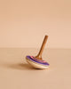 The Mader Bonbon Spinning Top - Purple showcases a purple and pink pattern, elegantly balanced on its point against a beige background—an embossed, classic wooden toy inspired by Austrian craftsmanship.