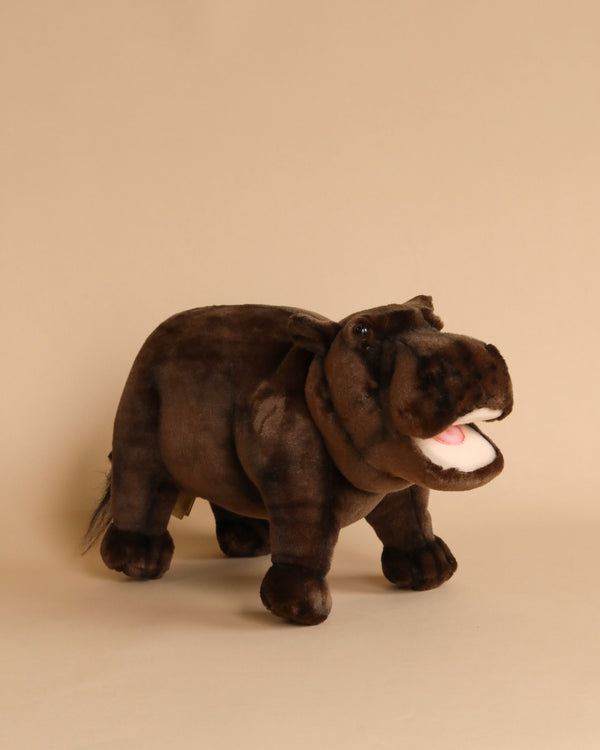 A Happy Hippo Stuffed Animal, artisan crafted and standing upright on a beige background, featuring a soft, brown fabric body with a slightly open mouth and visible white teeth.