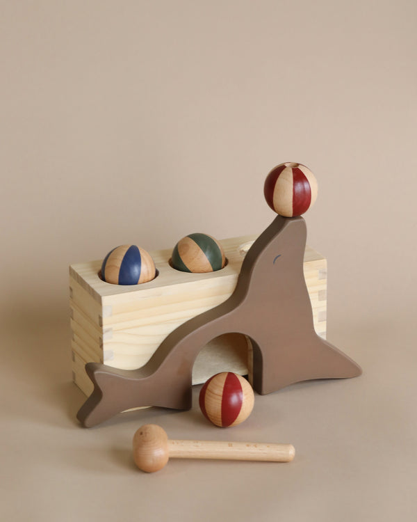 Wooden Hammer Game - Sea Lion set featuring a sea lion-shaped stacking game with colorful balls balanced on pegs and a box with more balls next to a small toy hammer on a neutral background, all crafted from FSC-cert