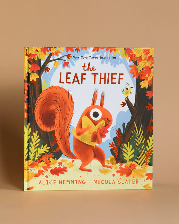 The Leaf Thief Book" by Alice Hemming and Nicola Slater features a vibrant cover with a red squirrel holding a leaf, standing among colorful autumn trees with falling leaves. The illustrated pages highlight a small bird perching nearby, set against the backdrop of a clear blue sky.