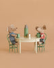 The Maileg Little Brother and Sister Dining Set features two mice in striped shirts sitting on green chairs at a vintage dining table with green mugs, a miniature thermos, and cup, all against a beige background.