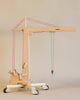 The Fagus Wooden Crane, handcrafted in Germany, showcases a meticulously designed wooden crane equipped with a lifting arm and red pulley strings mounted on a four-wheel base. The extending crane arm holds aloft a small wooden container filled with tools. This charming wooden toy stands out beautifully against a neutral backdrop.