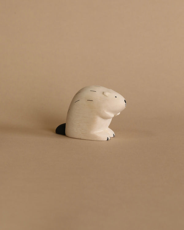 A small, handcrafted wooden figurine of a Handmade Wooden Beaver lying on its back, with a smooth, rounded body and minimalistic features, set against a plain tan background.